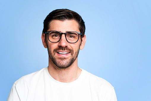 Portrait of a smiling man in white t-shirt and eyeglasses, isolated on a teal background