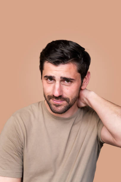 istock Pensive man with hand on neck against beige background 2129497838