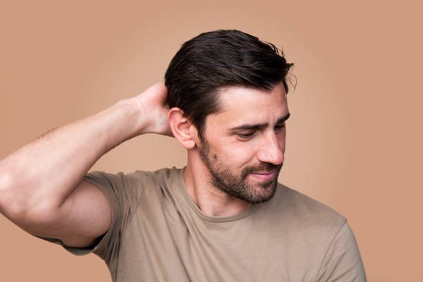 Thoughtful young man scratches his head, looking slightly confused or unsure