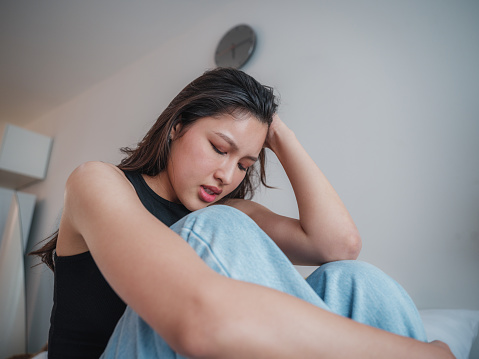 Portrait of upset Asian women feel strain or tired from mental health illness, Exhausted tired Asian women suffering stress and headache sitting in the bedroom at home