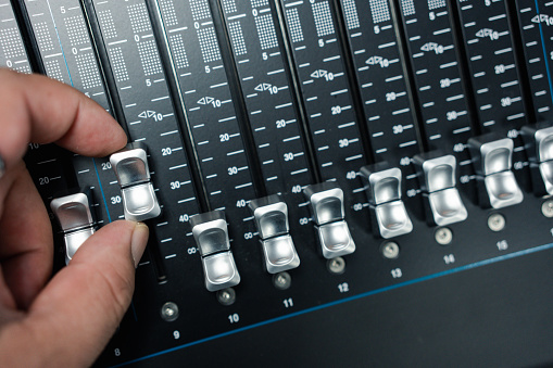 Human hand adjusting buttons on audio mixer. Professional audio mixing console