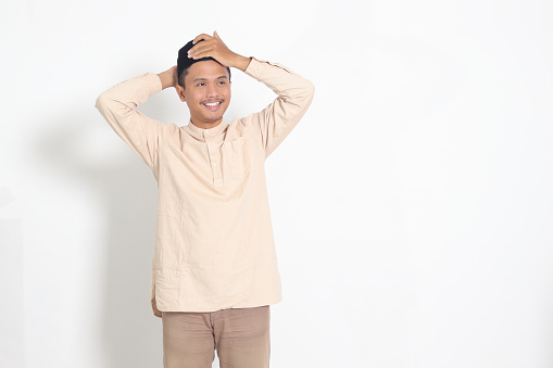 Portrait of excited Asian muslim man in koko shirt trying to adjust his songkok or peci or black skullcap. Isolated image on white background