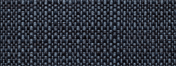 Texture of dark denim color background from woven textile material with wicker pattern, macro. Structure of vintage black fabric cloth, narrow backdrop.