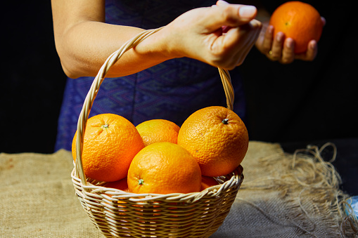 Cropped hand of woman holding ripe orange fruit in wicker basket