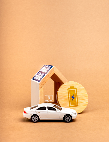 Sustainability at home concept. Battery power charging icon on round wood panel near solar panels being installed on home roof and white EV car with plug-in symbol, on recycle paper background.