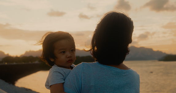 Asian mother holds son up to watch the sunset at the dam. traveling lifestyle.
