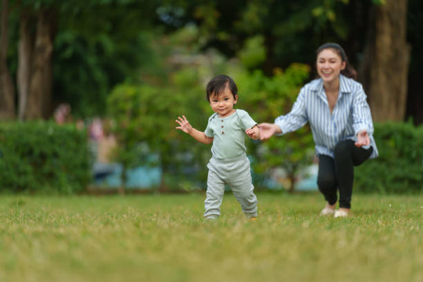 istock infant baby learn walking first step on grass field with mother helping in park 2129526883