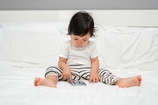 toddler baby using smartphone on a bed
