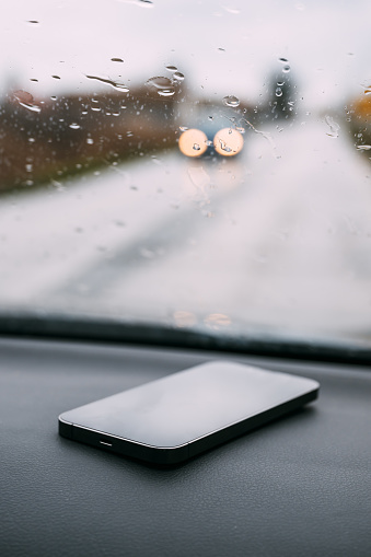 Smart phone on car dashboard on rainy day, selective focus