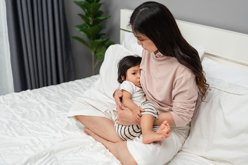 mother feeding breast her toddler baby on a bed