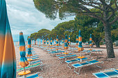 Folded beach umbrellas and empty deck chairs on town beach in Crikvenica, Croatia. Overcast weather and cloudy days during poor touristic season.