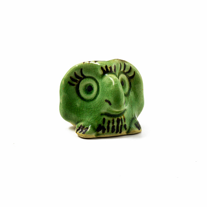Ceramic souvenir in the form of a small green owl on an isolated surface. Drawn black eyes, large beak. Cracks are visible in the glaze.