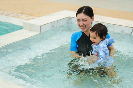 happy mother holding baby in her arms while playing in a swimming pool