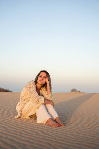 istock Happy young woman sitting on sand terrain 2129599623