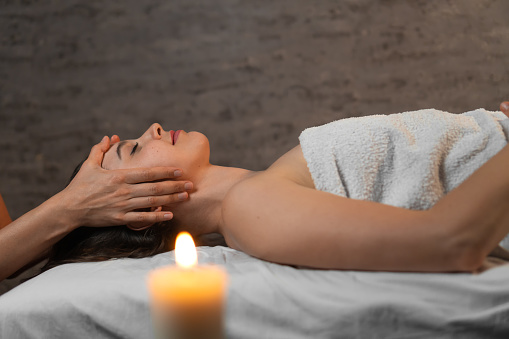 Young beautiful woman in a spa salon on a relaxing facial massage, a blurred candle in the foreground. Concept of health, body care and mental state