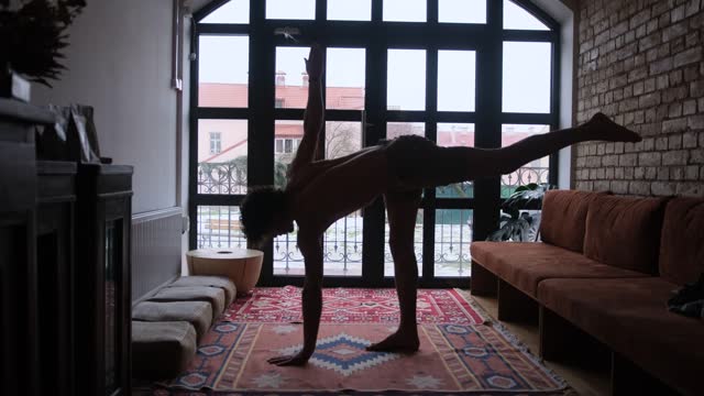 the silhouette of a handsome man practicing yoga against the background of a large window in the room.