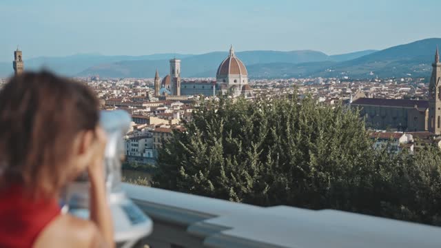 Visiting the viewpoint in Florence. Rear view of a pretty asian girl looking through binoculars at the Cathedral of Santa Maria del Fiore. Beautiful young brunette enjoying the city view.