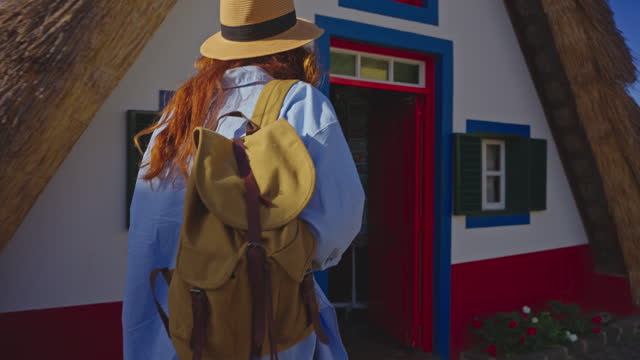 A girl travels in a hat and with a backpack and visits extraordinary traditional A-shaped houses in Santana in Portugal Madeira