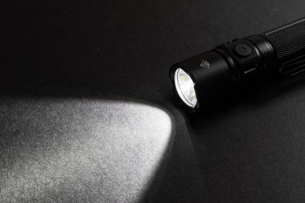 istock Flashlight and a beam of light in darkness. A modern led lamp with bright projection on dark wood table. 2129720262