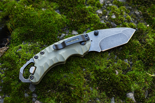 Tactical folding knife for survival on moss background.