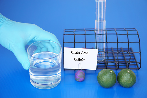 Science experiment about Citric Acid with molecular formula C6H8O7. Hand in blue glove hold glass of water, test tube and lime fruits. Concept, Education, Science laboratory lesson.