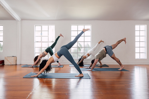 Small mixed class doing exercises at a modern yoga studio gym. Small group of people men and women of different ages practicing mindfulness and yoga lesson.