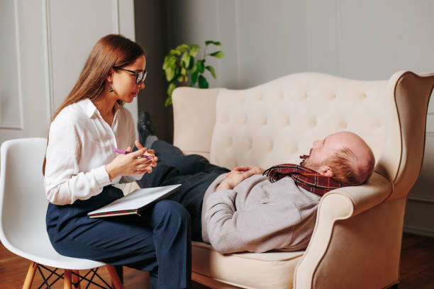 Elderly male client of psychotherapy woman relaxed lying on couch in office, girl says. Elderly male client of psychotherapy woman relaxed lying on couch in office, girl says. Psychological session, consultation of psychologist, comfortable posture conducive to confidential conversation. neuropsychology stock pictures, royalty-free photos & images
