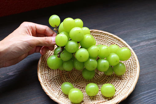 Hand Placing Bunch of Bright Green Ripe Shine Muscat Grapes in a Basket