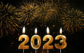 Golden holiday candles 2023 are burning on background of gold fireworks. Happy new year 2023, creative idea