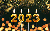 Amazing golden candles 2023 burn on a dark background with golden fireworks, gold confetti and bokeh lights. Happy new year card creative idea