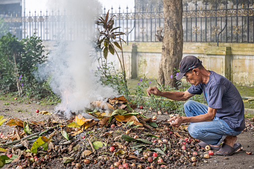 Medan, Sumatra, Indonesia - January 16th 2024: Man burning dried leaves in a public park in the center of the main city on Sumatra