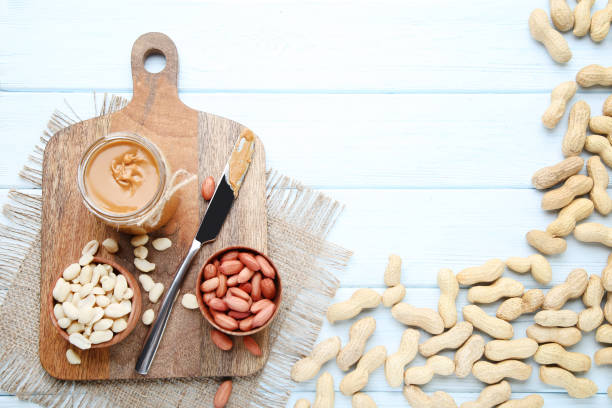 istock Peanut butter and nuts with knife and cutting board on wooden table 2129804880