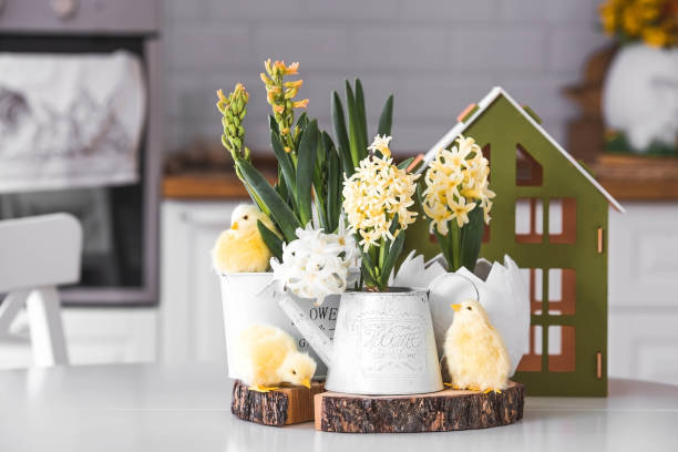 Happy Easter. Spring yellow hyacinth flowers in an egg-shaped vase, chicken chicks on a white table. In the background is a white Scandinavian-style kitchen. Easter decor in the house.