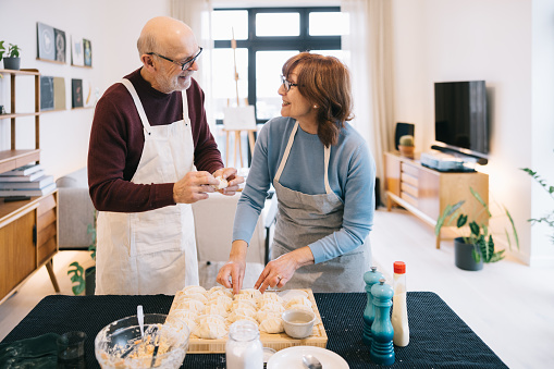 A senior couple shares a tender moment in the kitchen as they lovingly prepare homemade gyozas together, their hands expertly folding and filling dumplings with care