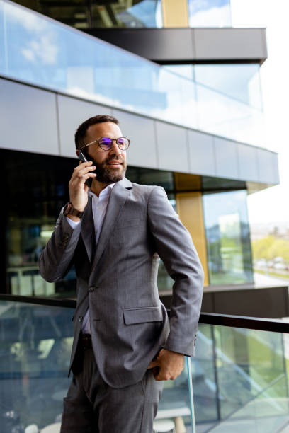 istock Confident Businessman Smiling in Sharp Suit Against Modern Glass Office Facade 2129851357