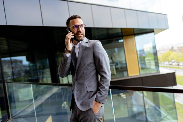istock Confident Businessman Smiling in Sharp Suit Against Modern Glass Office Facade. Generative AI 2129851361