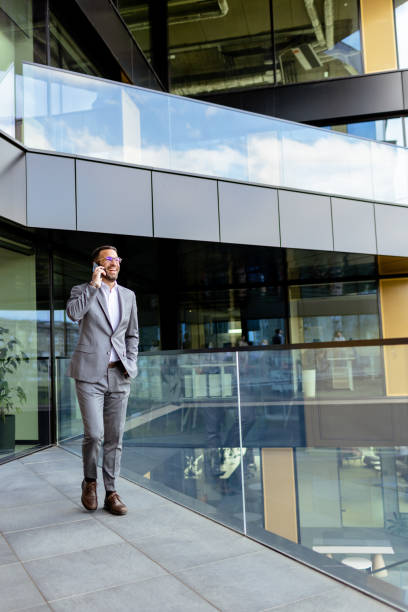istock Confident Businessman Smiling in Sharp Suit Against Modern Glass Office Facade. Generative AI 2129851547