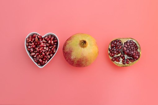 Pomegranate seeds in heart shape bowl on red background.
