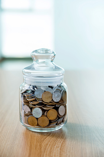 Coins in a jar on wooden table.