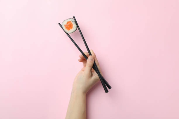 istock Female hand hold chopsticks with maki on pink background 2129873640