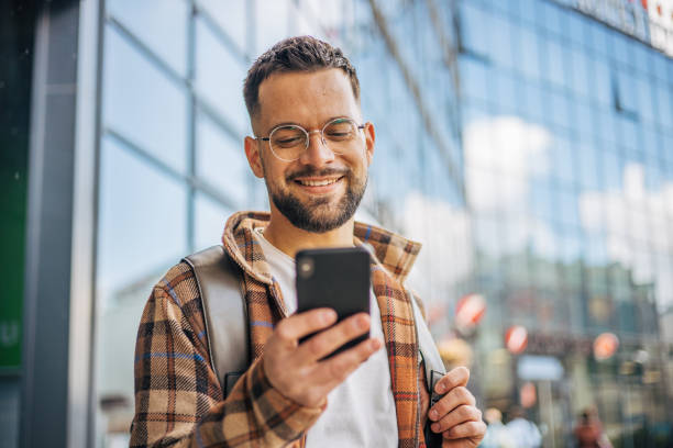 A smiling adult man walked out of the office building after finishing work. A smiling adult man walked out of the office building after finishing work. He is standing outside using his smartphone. happy using phone stock pictures, royalty-free photos & images