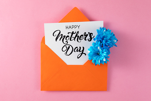 Mother’s Day concept with flowers in orange colored envelope with greeting card on pink background