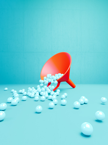 Coral colored funnel filled with spheres before blue background. Vertical composition. Big data and marketing concept.