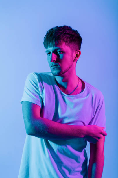 istock Handsome creative young hipster man with hairstyle in white t-shirt poses in studio with colored neon pink light 2129921521