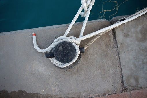 yacht is tied with a white rope to a metal bollard in the port, top view. Safety and support concept. Boat docked in the port