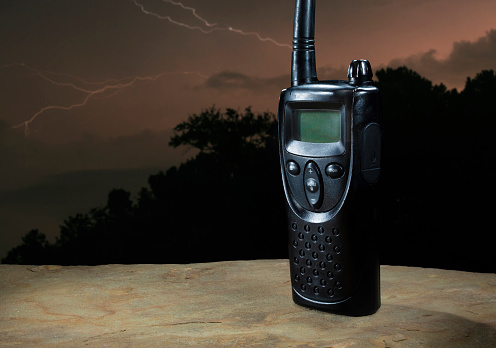 Handheld two way radio with a lightning storm behind with a screen that is blank for inserting copy