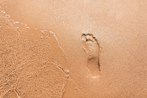 Human footprint in the sand on the beach with a wave near the sea, top view. Summer vacation and rest concept