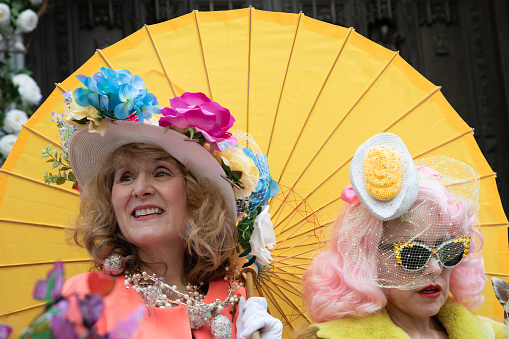 New York City, NY- Two woman in Easter themed costumes, pose in front of a giant yellow, fan, during the annual Easter Bonnet Parade in NYC.
