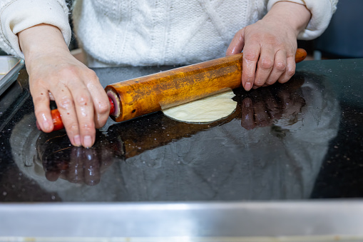 old woman hands using rolling pin to flatten the dough  on black marble  covered with oil