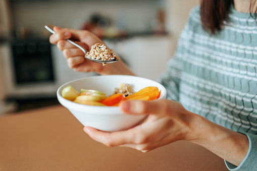 Unrecognizable female hands hold a plate of granola porridge and a full spoon while sitting in the kitchen. Diet prescribed by a nutritionist. healthy breakfast, healthy food. Healthy food concept.